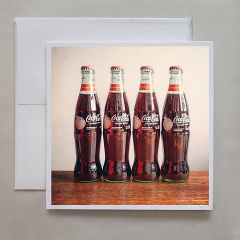 This greeting card features four, vintage coca cola bottles standing in a row by photographer Jennifer Echols. 