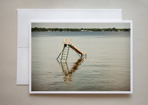 A summer photograph of a large yellow and green child's slide in the waters of DeGrassi Point, Lake Simcoe by photographer Caley Taylor.