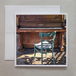 I love outside, public pianos!  This notecard shows a green chair covered in grated, side lighting with the brown, worn piano in the background by Jennifer Echols.
