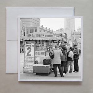 The black and white, film photograph is an urban, downtown Toronto shot of customers standing around Mrs Dalloway's hot dog stand by photographer Caley Taylor.